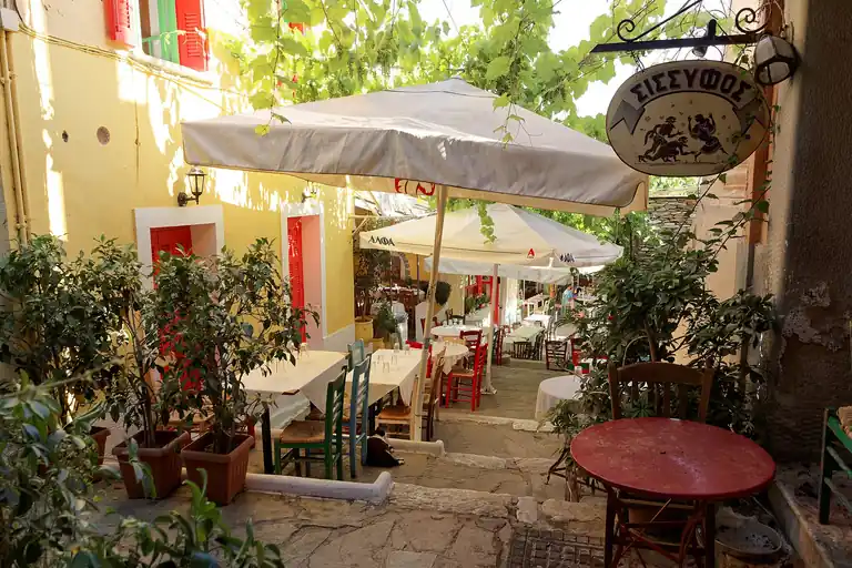 Taverna tables on the stepped Mnisikleous Street in Plaka, Athens, under a vine.