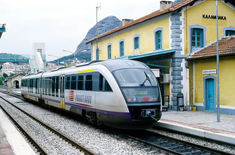 A regional train at Kalambaka station, the rock pillars rising behind the station building.