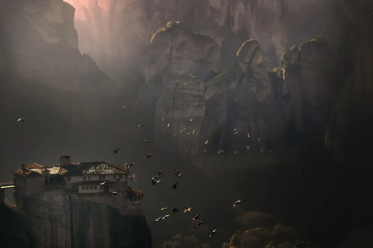 The monastery of Rousanou at Meteora in morning mist, with birds over the valley.