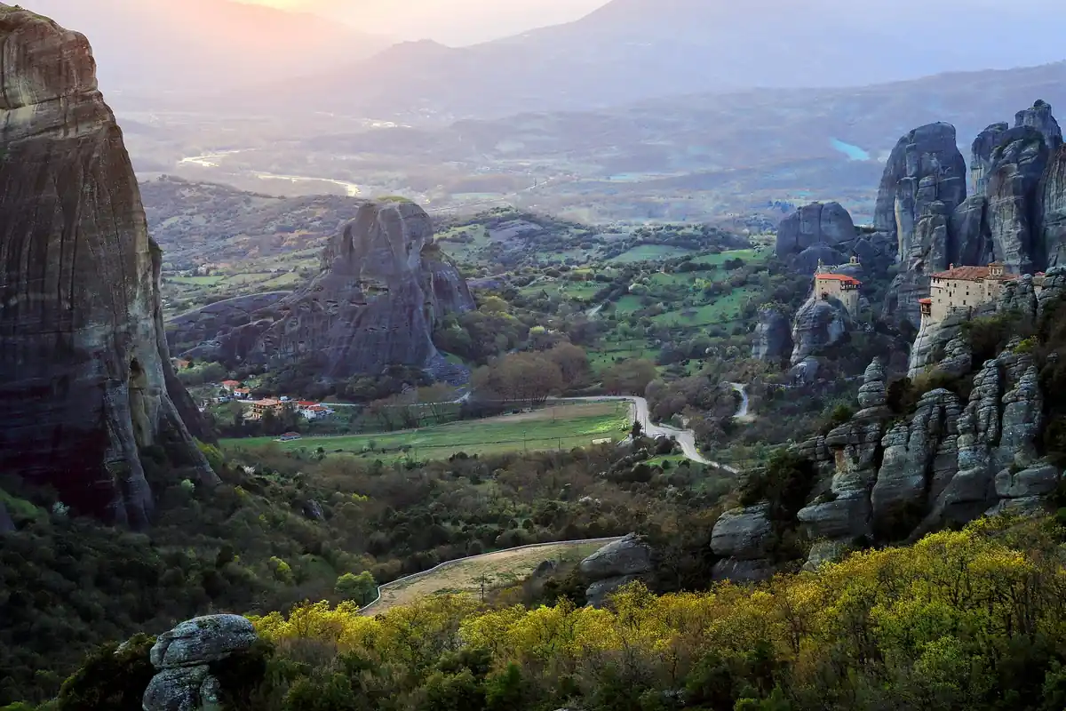 The valley of Meteora at dusk, with the pillars and a monastery above the fields.
