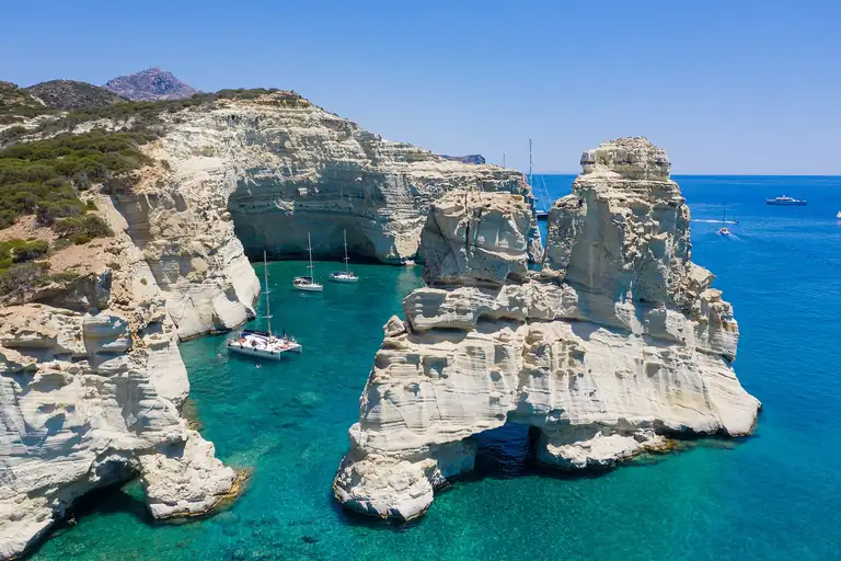 The white rocks and turquoise water of Kleftiko on Milos, with small boats at anchor.